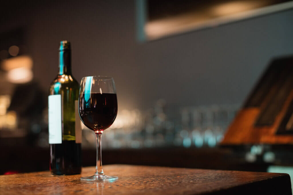 Eine Flasche Rotwein neben einem gefüllten Glas auf einem rustikalen Tisch im Hotel Sendlhof.