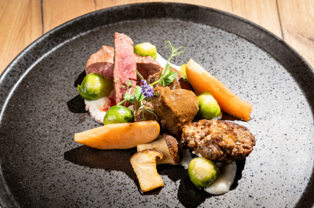Appetizingly arranged meat dish with Brussels sprouts, carrots, mushrooms, and creamy purée on a dark plate