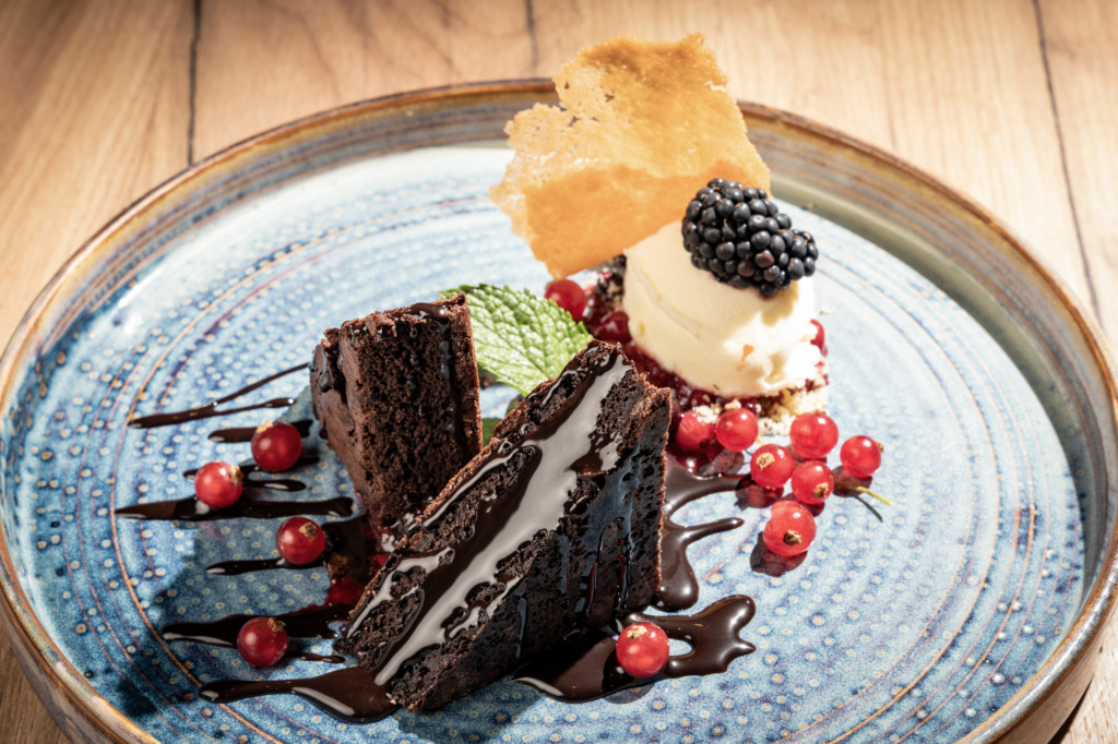 Chocolate cake with vanilla ice cream, blackberry, red currants, and chocolate sauce on a blue plate